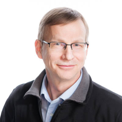 A man wearing glasses looks at the camera and smiles.