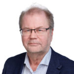 Silmälasipäinen mies katsoo kameraan ja hymyilee.