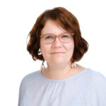 A woman wearing glasses looks at the camera and smiles.