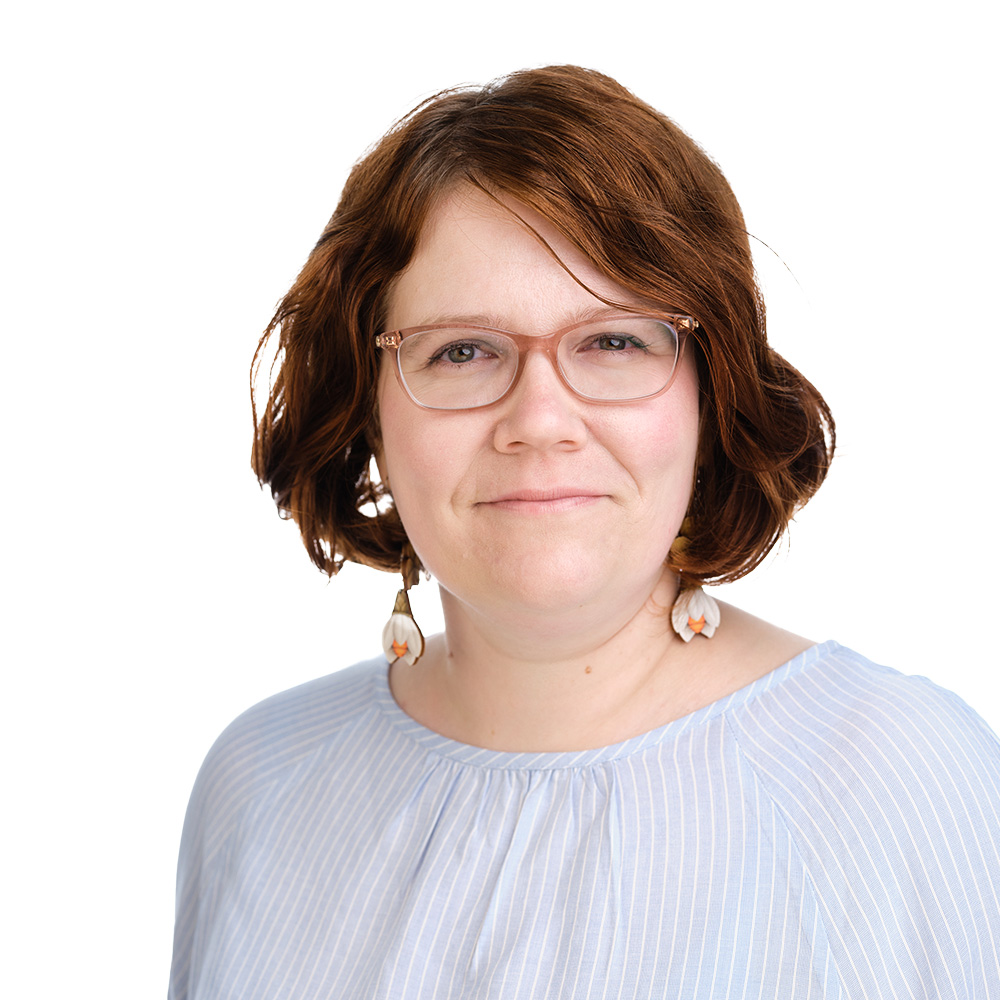 A woman wearing glasses looks at the camera and smiles.