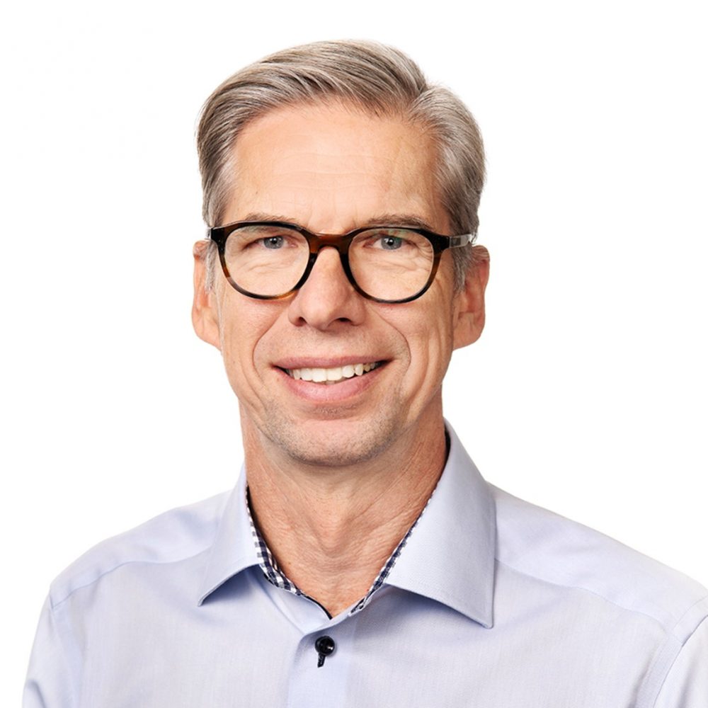 A man wearing glasses looks at the camera and smiles.